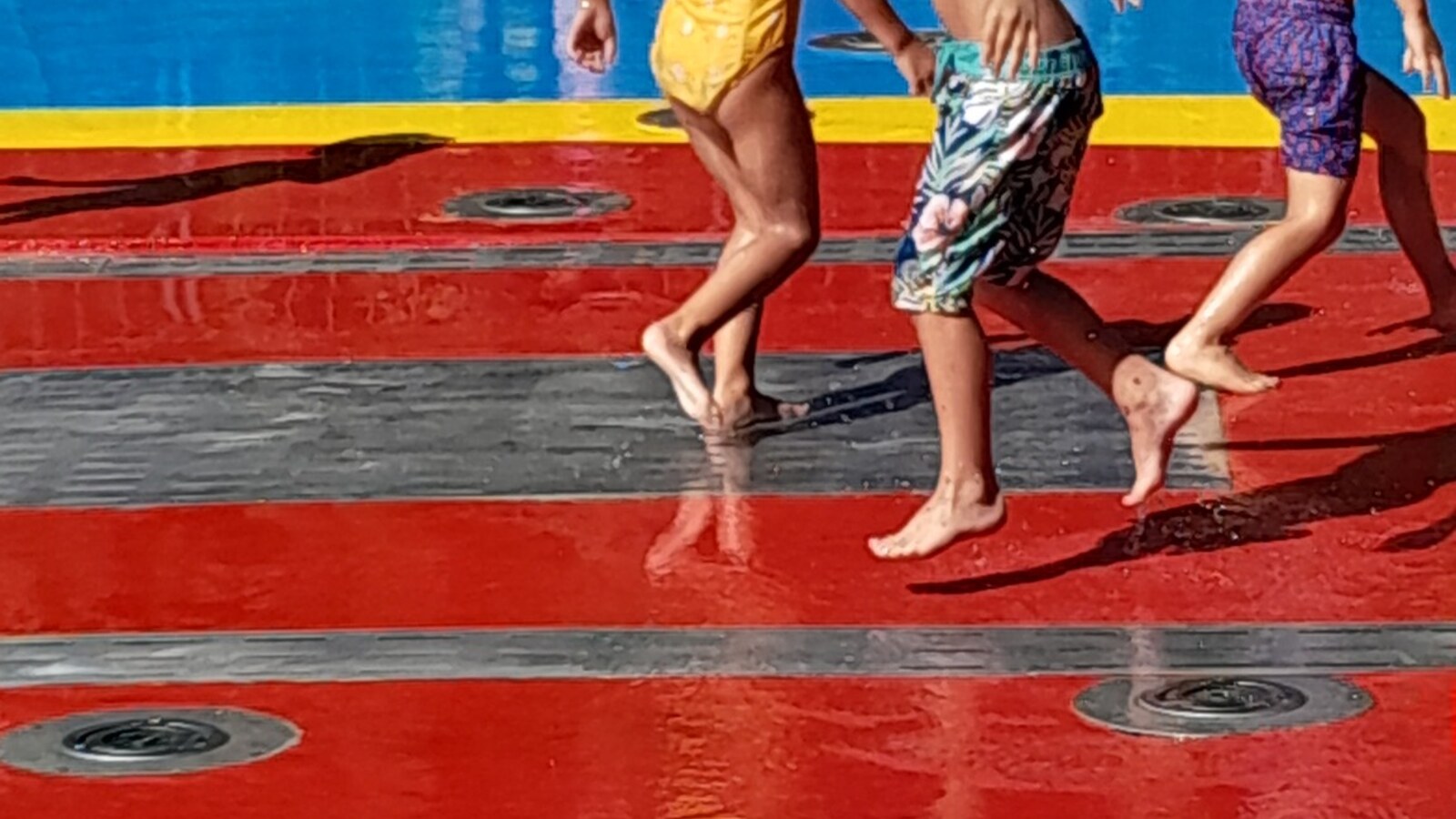Children running barefoot through a large colorful public splash pad in Santiago, Chile.