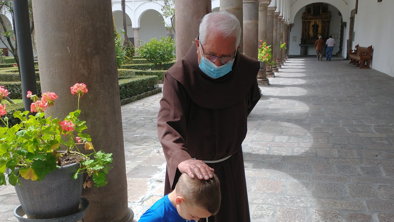 A Franciscan friar resting his hand on Sam’s head in a historic courtyard in Quito, Ecuador.