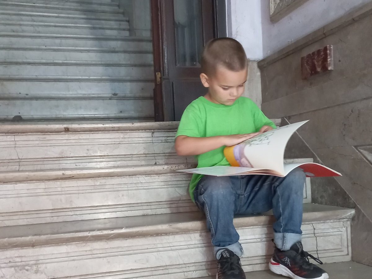 Samuel at age eight sitting on a staircase and pretending to read a book independently.
