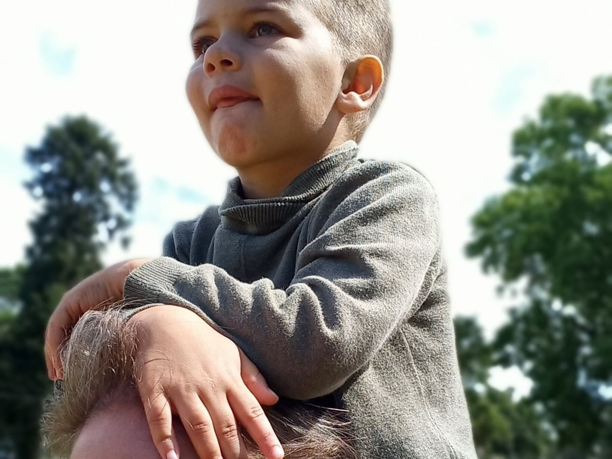 Samuel sitting on his mother's shoulders outdoors in Paraguay.