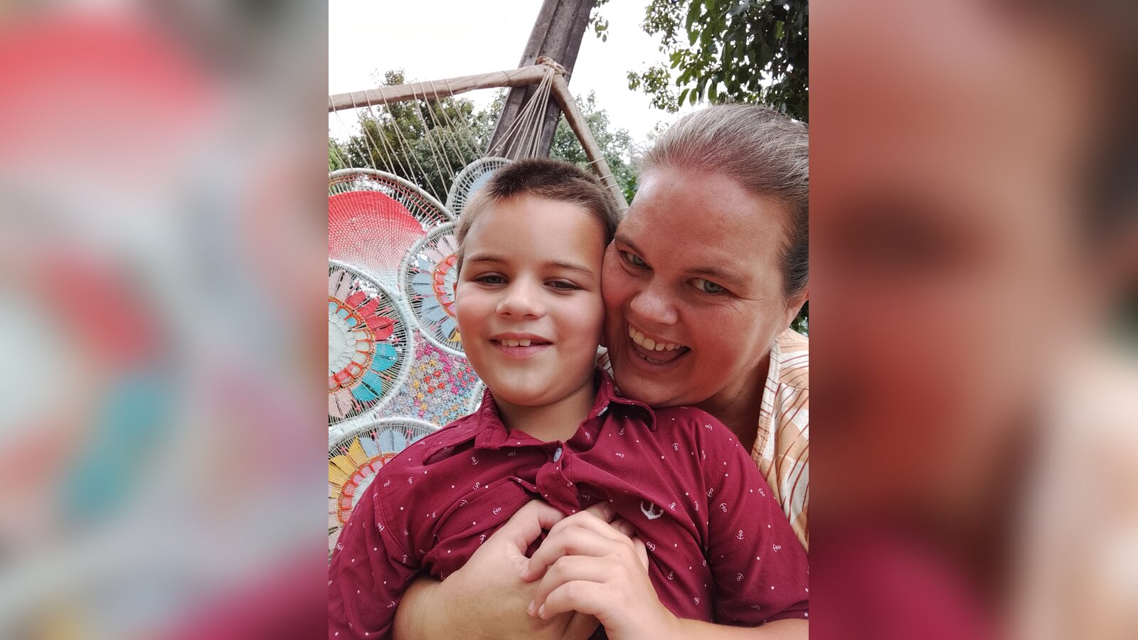 Amie and Samuel smiling together in Itauguá, Paraguay, with colorful traditional ñandutí lace displayed behind them.