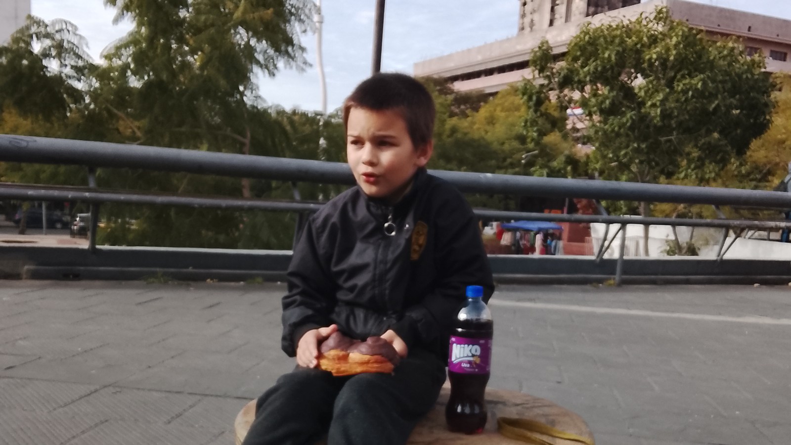 Sam in a dark jacket seated on a colorful play structure, holding food during an outing.