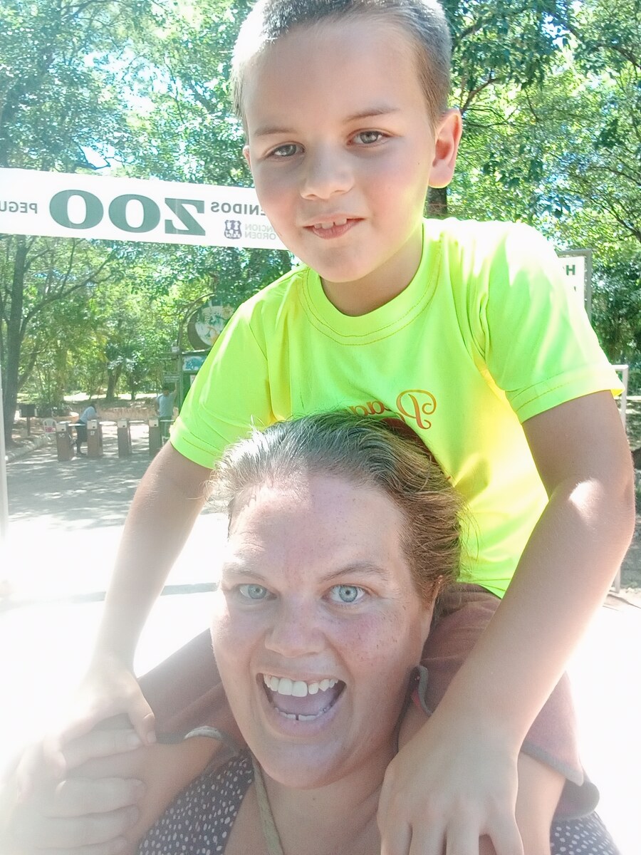 Amie smiling with Sam on her shoulders in front of the zoo entrance sign in Asunción.