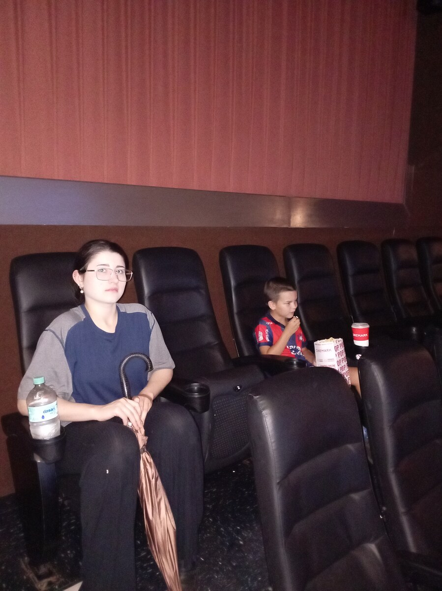 Monica and Sam seated in a cinema, with Sam eating popcorn from a tub beside him.