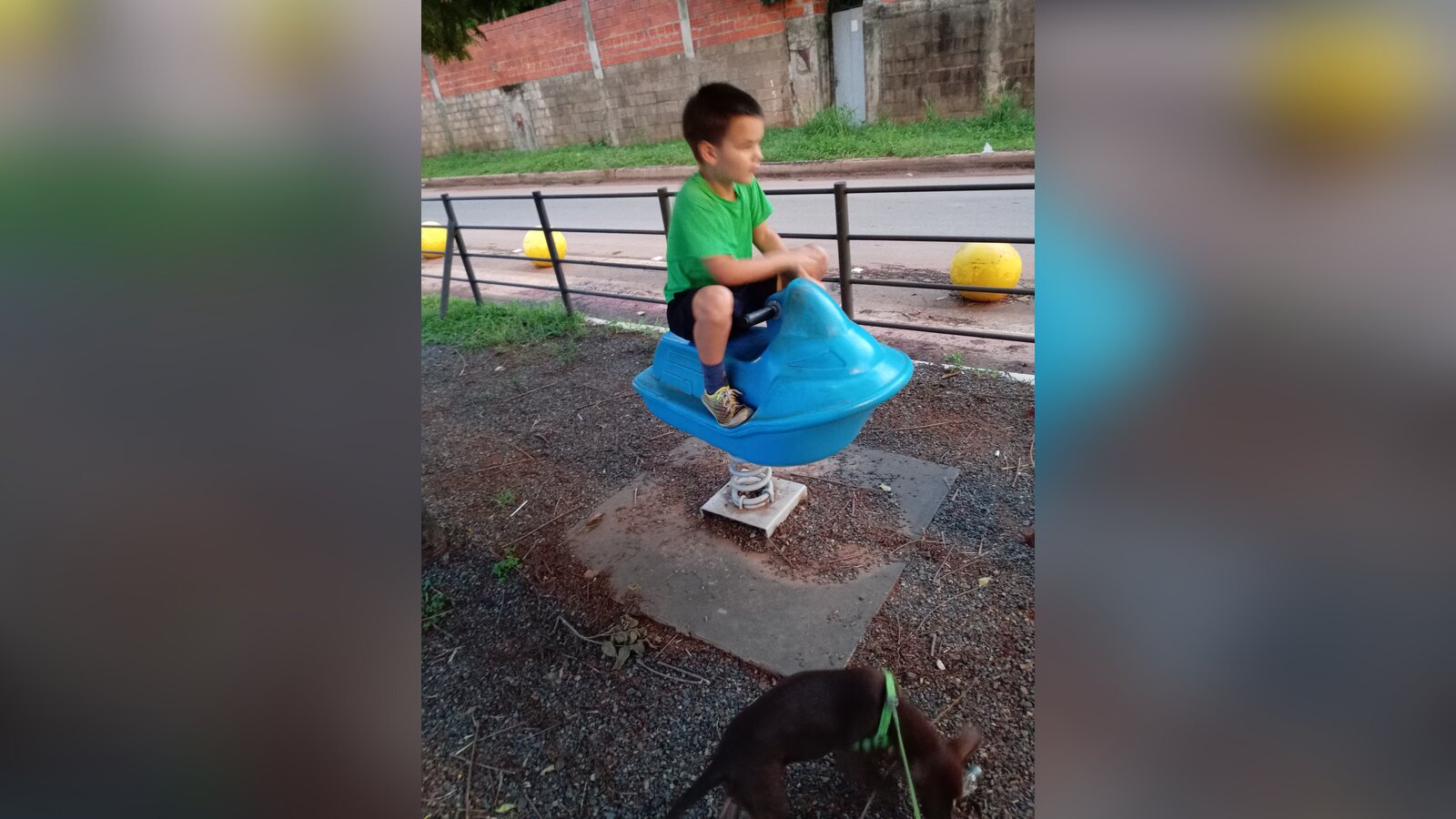 Sam playing on a blue spring rider in San Lorenzo, Paraguay, with a metal guardrail between the playground and a busy street.