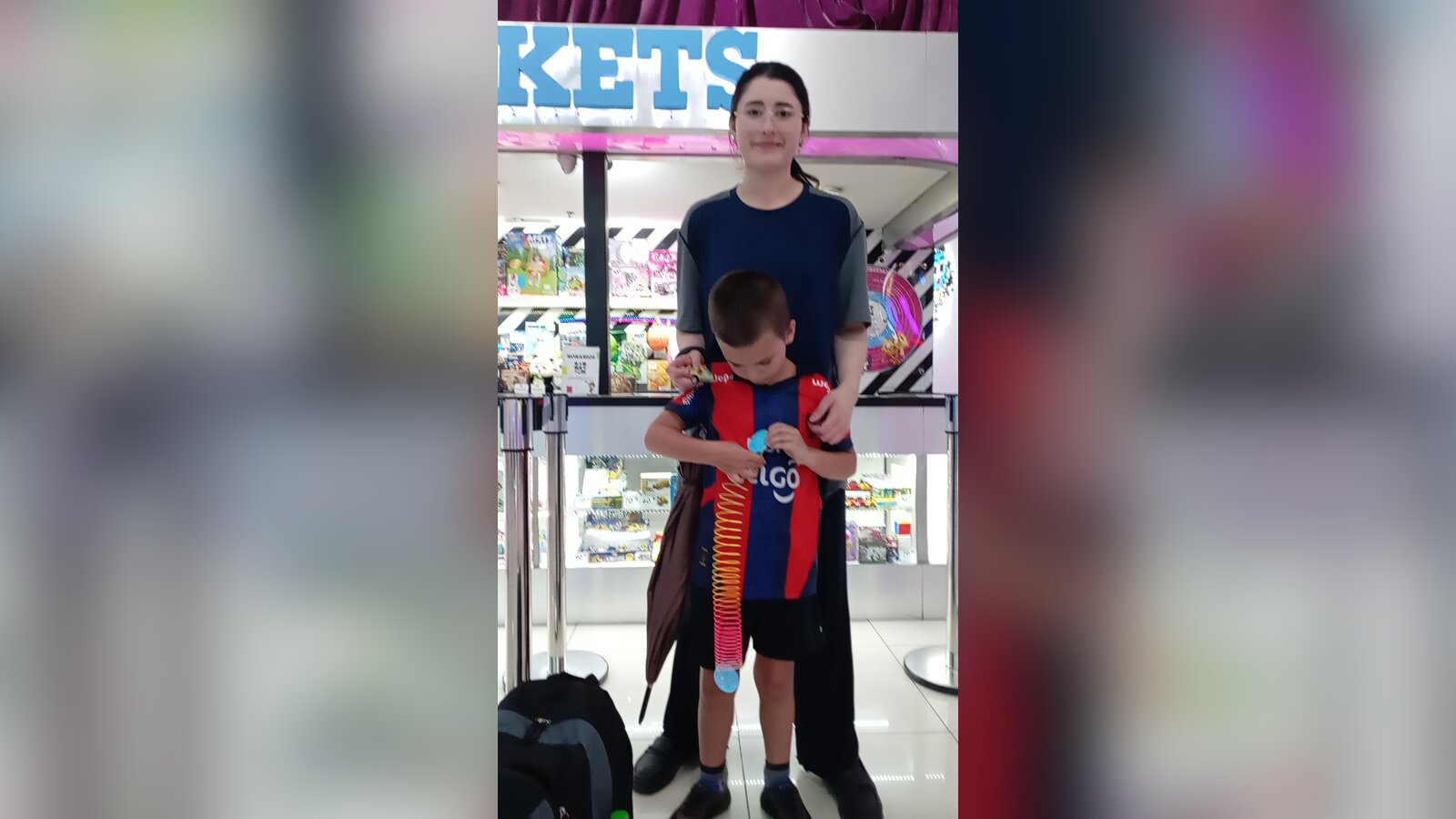 Sam holding a colorful spring toy with family friend Monica standing behind him near a game-and-prize counter.