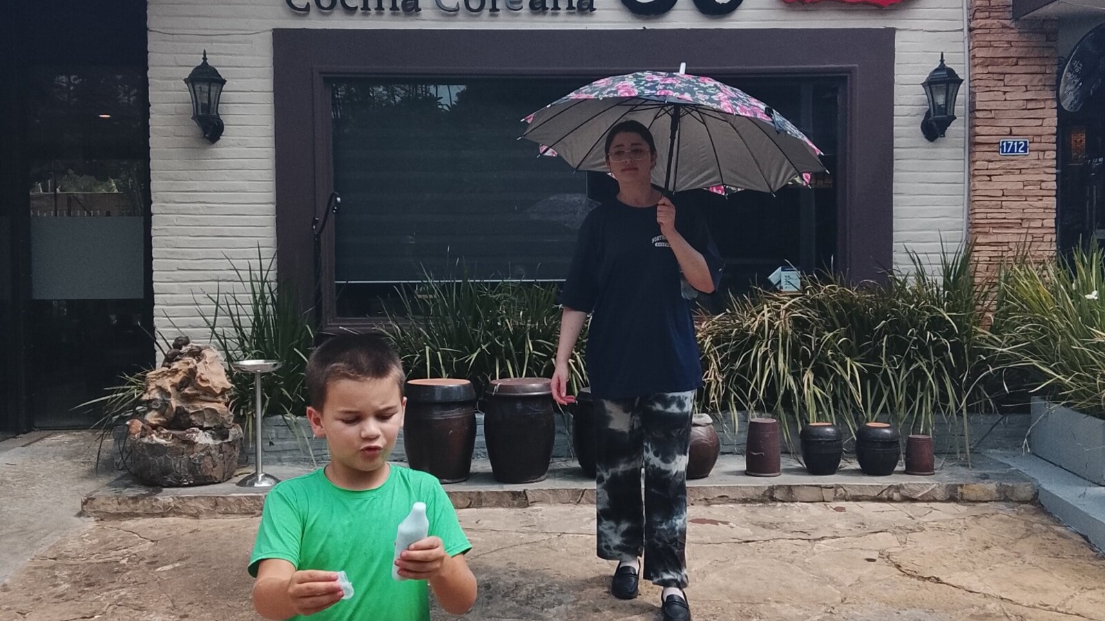 Sam walking toward the camera outside a Korean restaurant in Paraguay while an adult follows nearby.