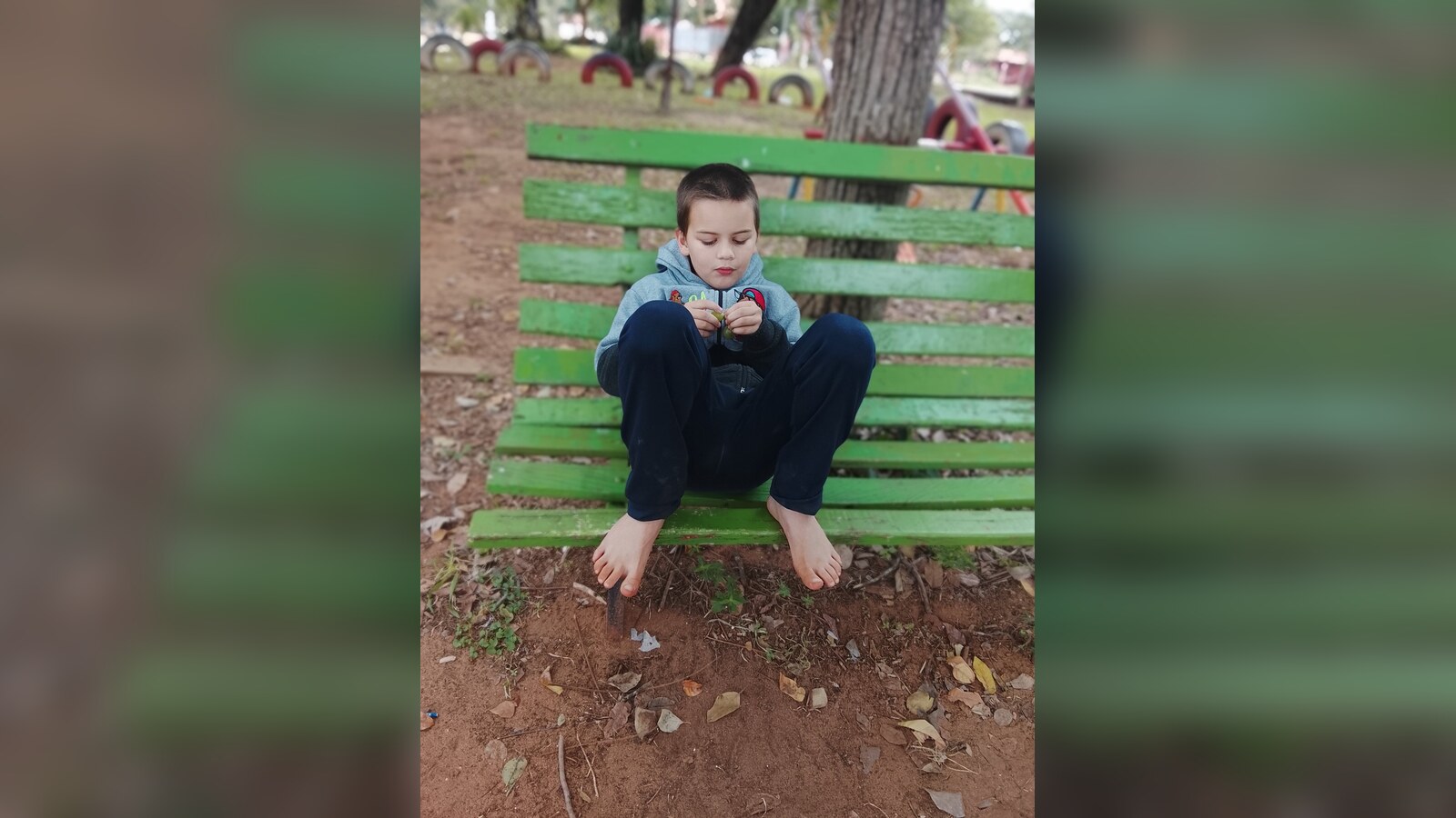 Sam sitting barefoot and quietly focused on a green bench during a morning walk in his neighborhood.