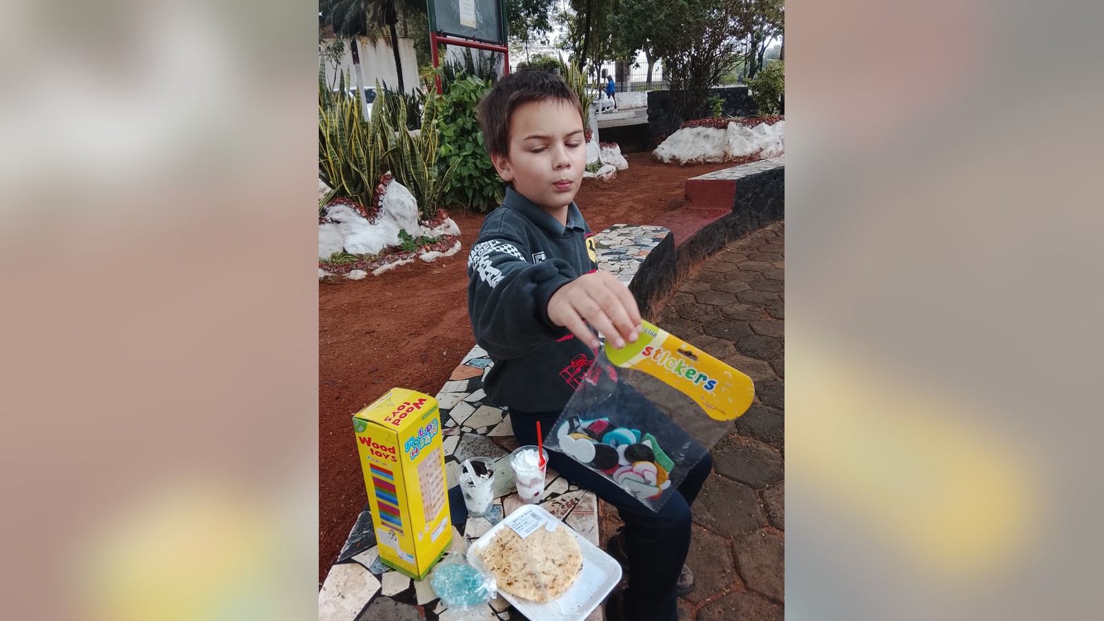 Sam holding up a packet of stickers beside snacks on an outdoor table.