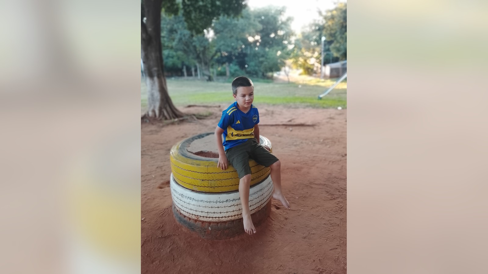 Sam sitting barefoot on a stack of brightly painted tires at an outdoor playground.